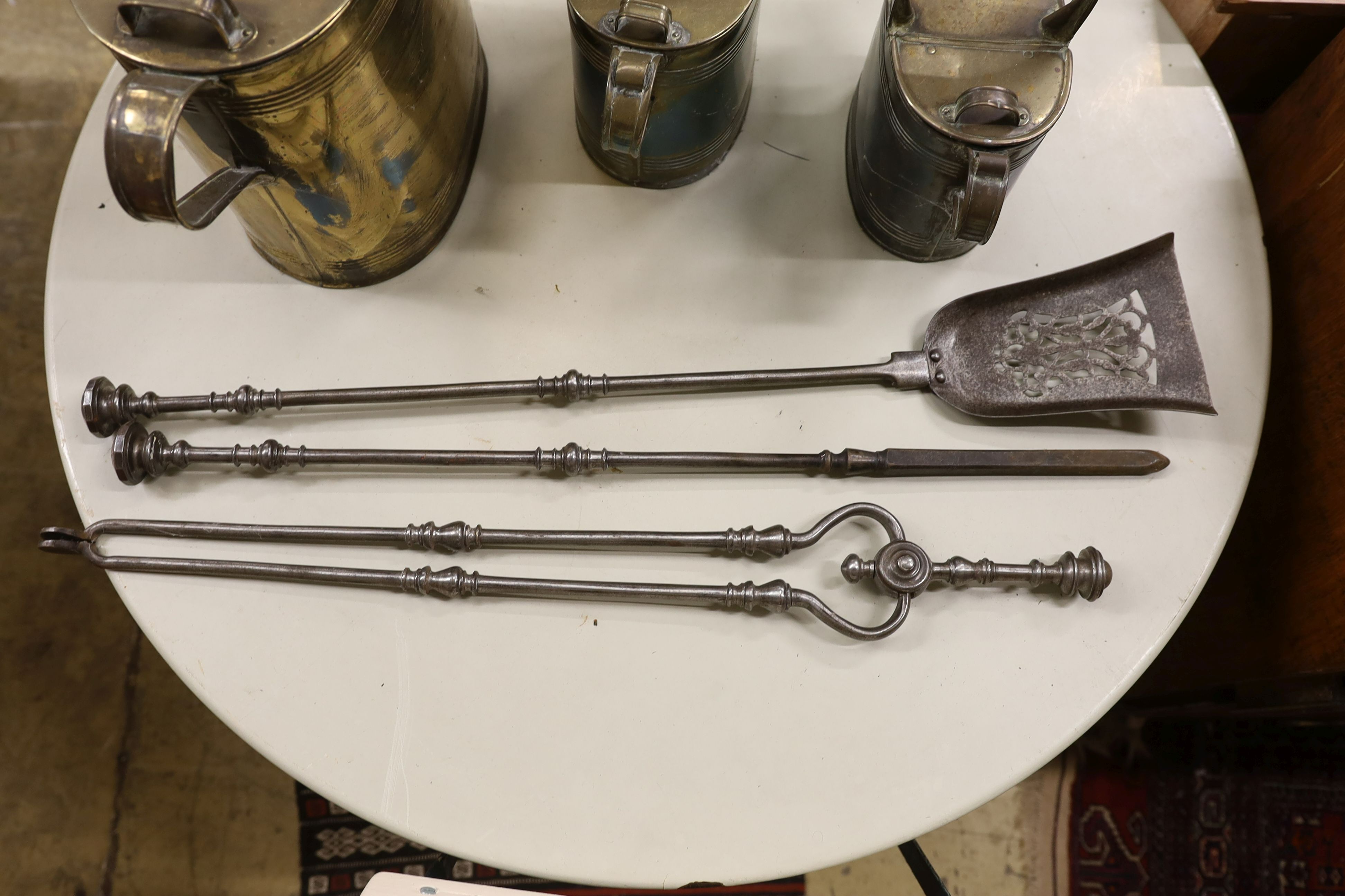 Three graduating brassed metal watering cans, largest height 40cm, together with a set of cast iron fire implements